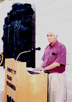 ד&quot;ר אברהם רוכלי, חבר הועד המנהל של אגודת קורצ&#039;אק בישראל, נושא דברים בטקס על רקע האנדרטה לזכרם של קורצ&#039;ק והילדים